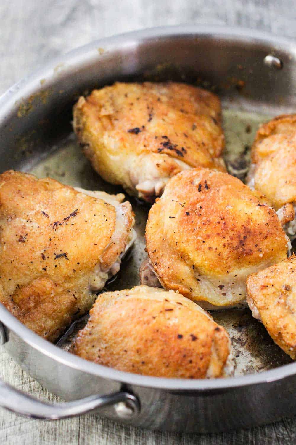 6 skin-on, bone-in chicken thighs that have been seared in a large silver skillet, skin side up.