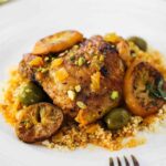 A white plate filled with chicken tagine with preserved lemons and olives with a fork resting on the plate.