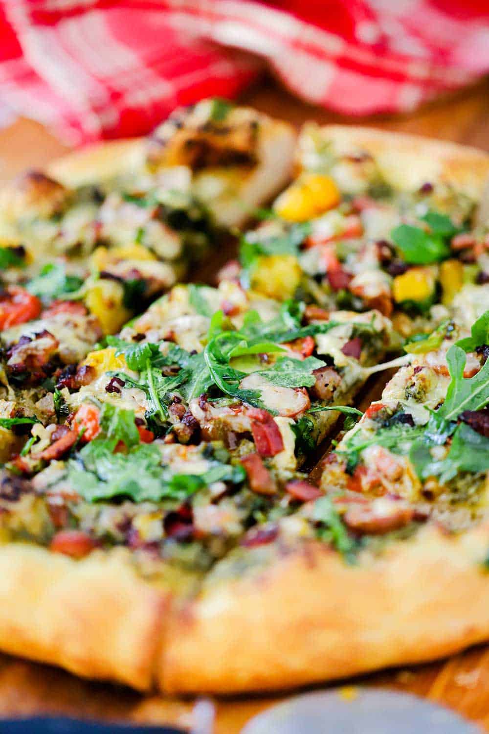 A close up view of a BLT pizza cut into squares next to a red checkered napkin.