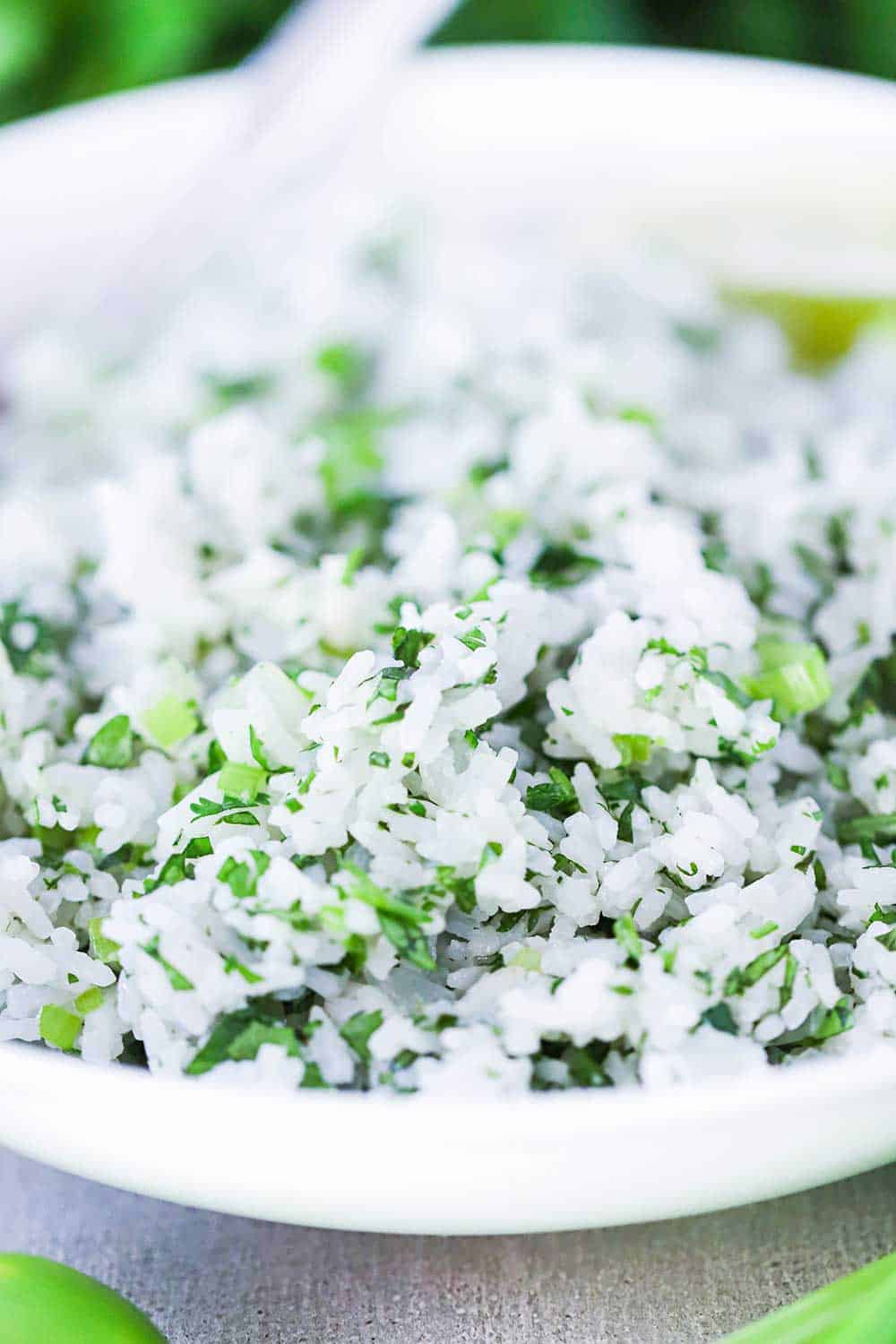 A close-up view of a white bowl filled with Cilantro Lime Rice with a silver spoon in it.