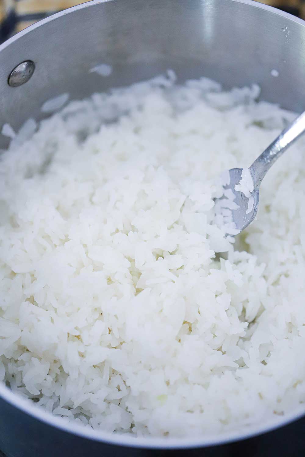 An overhead view looking down into a silver pan filled with fluffy cooked Jasmine rice with a fork in it.