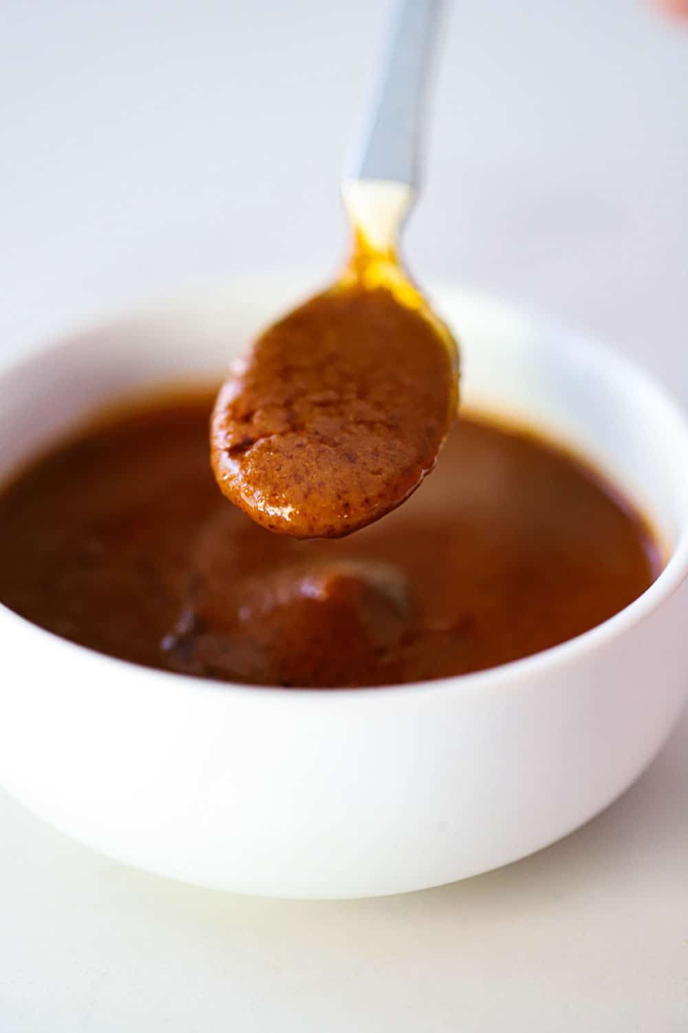A small white bowl filled with homemade steakhouse with a small spoon lifting some out of the dish.