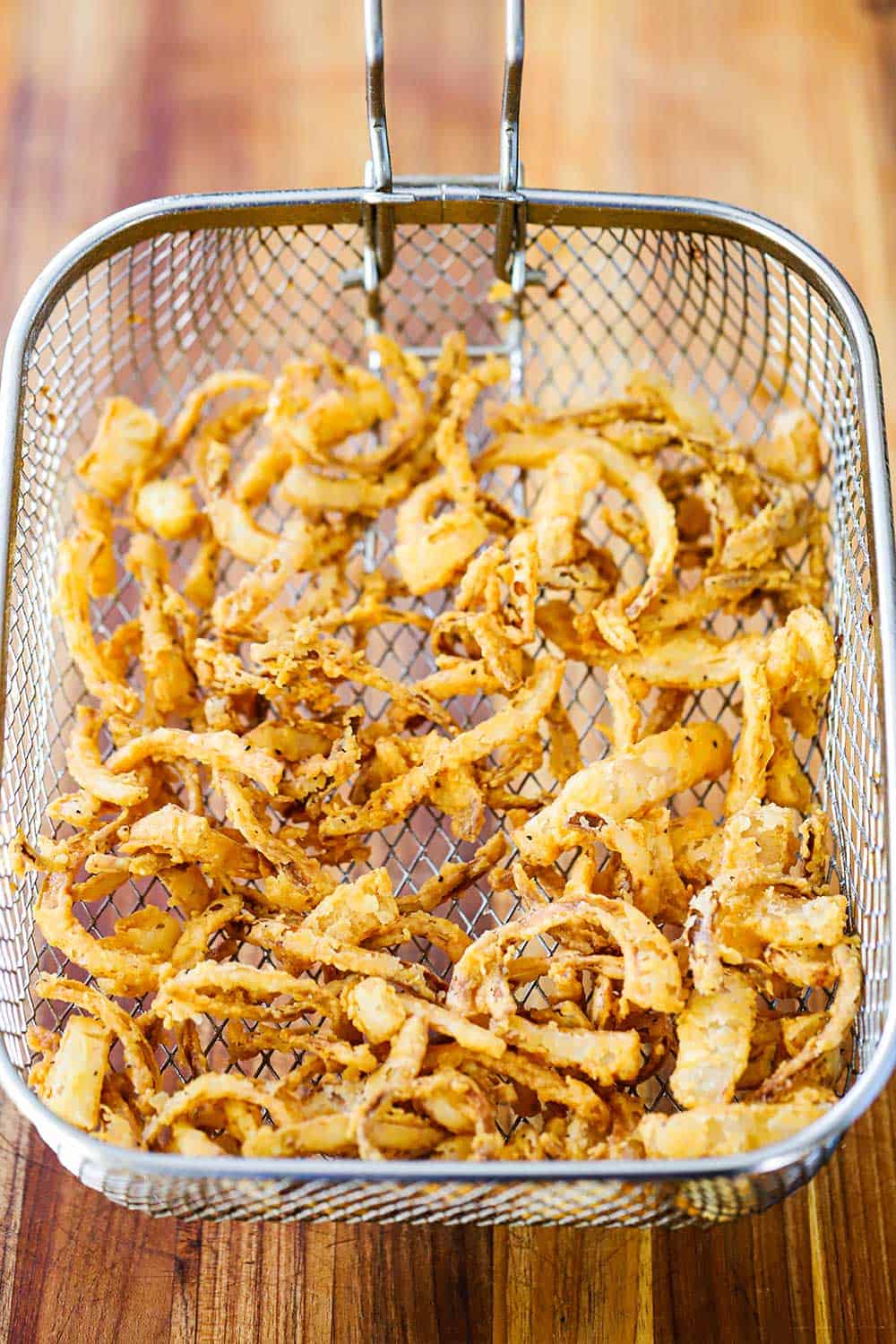 An overhead view of a deep-fryer basket filled with fried onion strips.