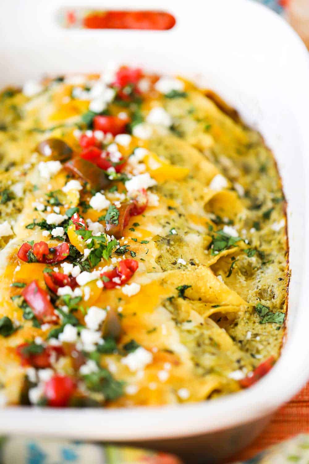 A close-up view of a white baking dish filled with chicken enchiladas with verde sauce.