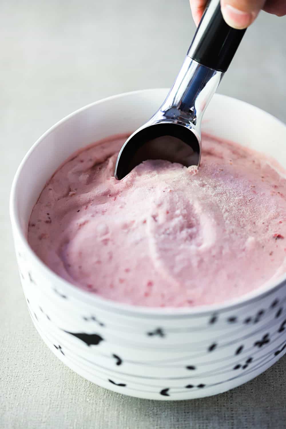 A ceramic bowl filled with homemade strawberry ice cream with an ice cream scoop stuck in it.