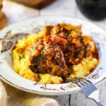 A close-up view of an antique bowl filled with polenta and Instant Pot Italian short ribs.
