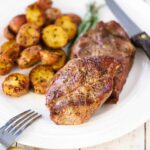A pork burger with a sliced of green lettuce under the patty and a slice of tomato on top all on a wooden cutting board.