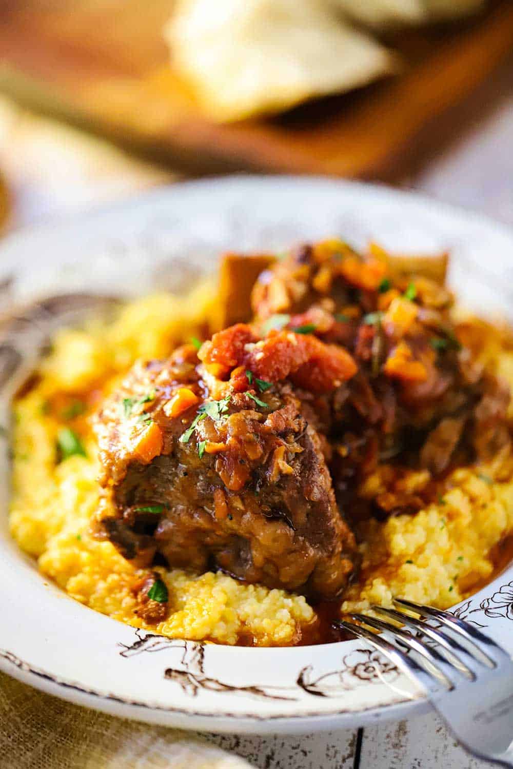 A close-up view of an antique bowl filled with polenta and Instant Pot Italian short ribs.