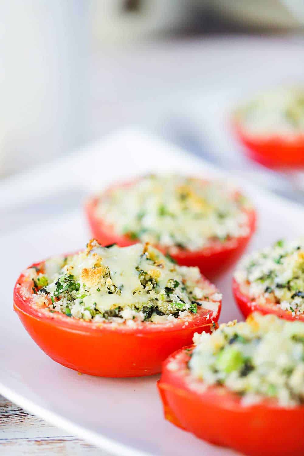 A close-up view of a tomato that is split in half and stuffed with toasted breading and herbs on a white platter.