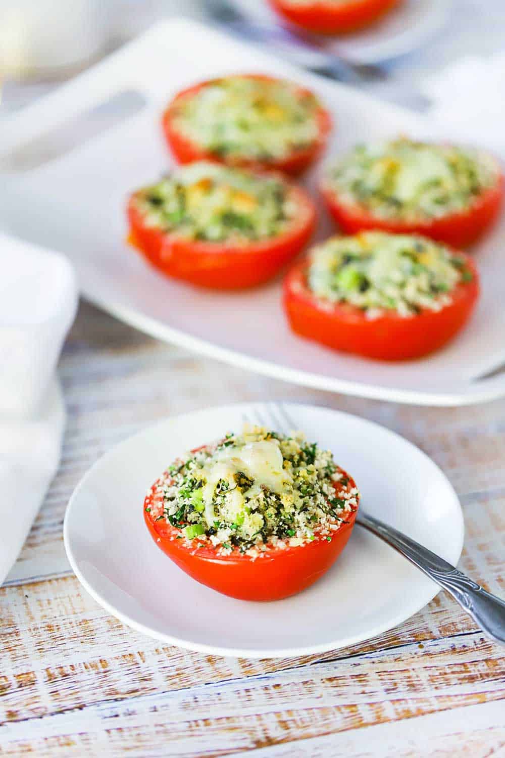 A tomato cut in half and filled with toasted herb bread crumb filling sitting on a white plate