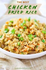 A close-up view of a white serving bowl filled with homemade chicken fried rice next to a gold spoon.