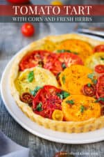 A tomato tart with colorful sliced tomatoes on top in a pastry shell all on a white serving plate.
