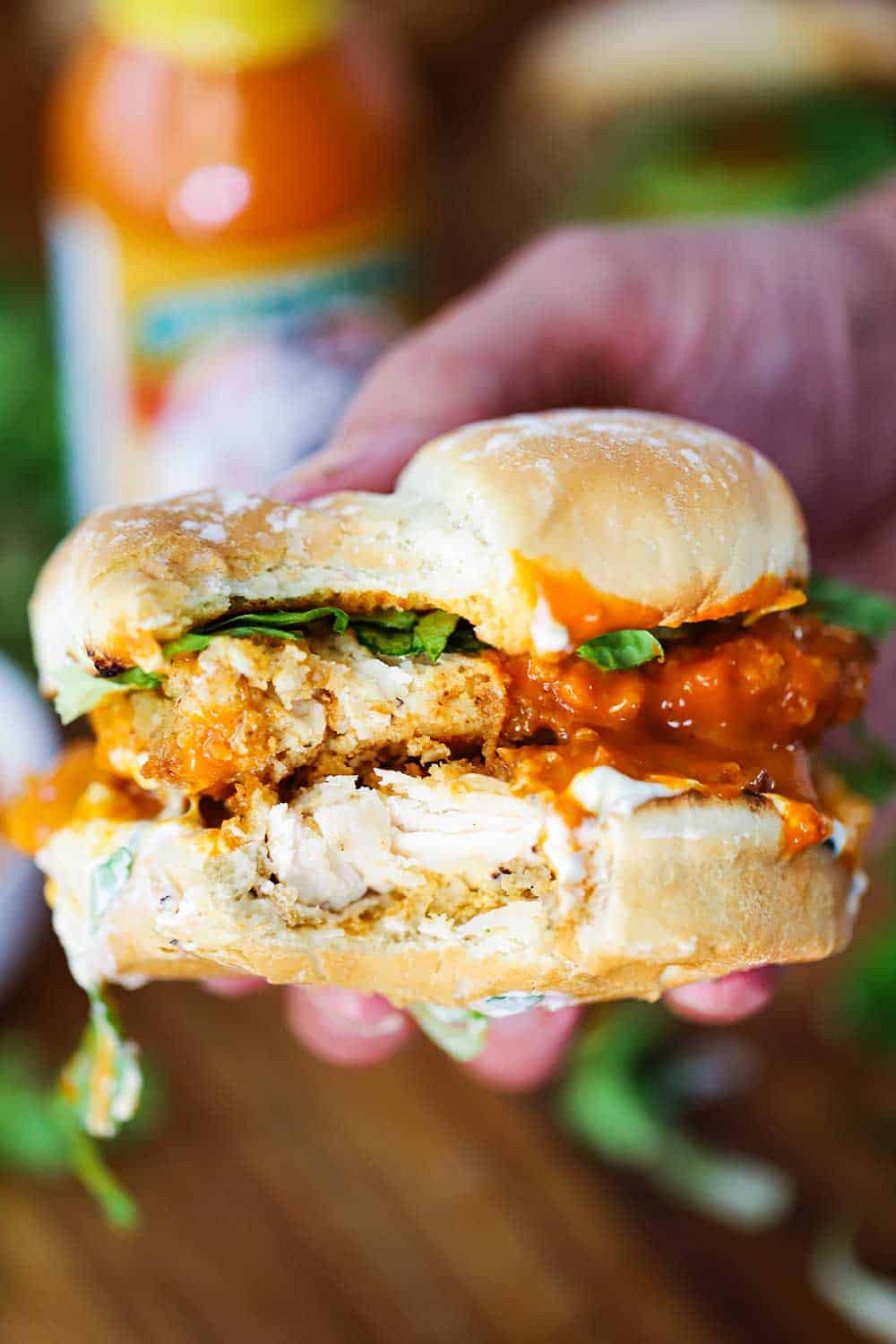 A hand holding a buffalo chicken sandwich with a bite taken out of it.