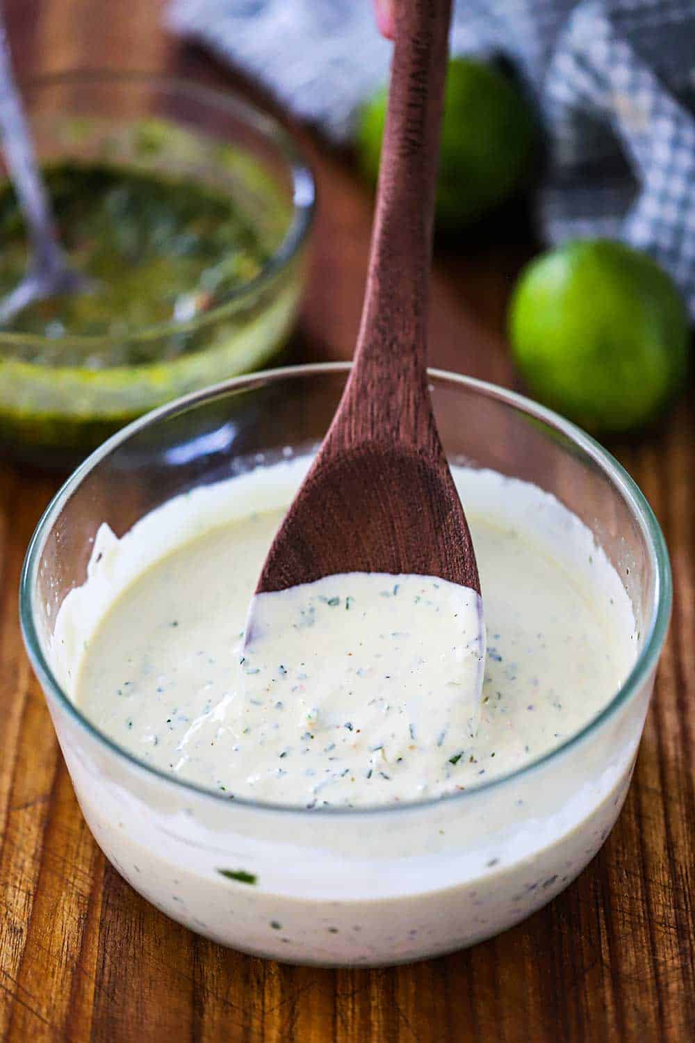 A glass bowl filled with chimichurri mayonnaise with a wooden spoon in the middle of it.
