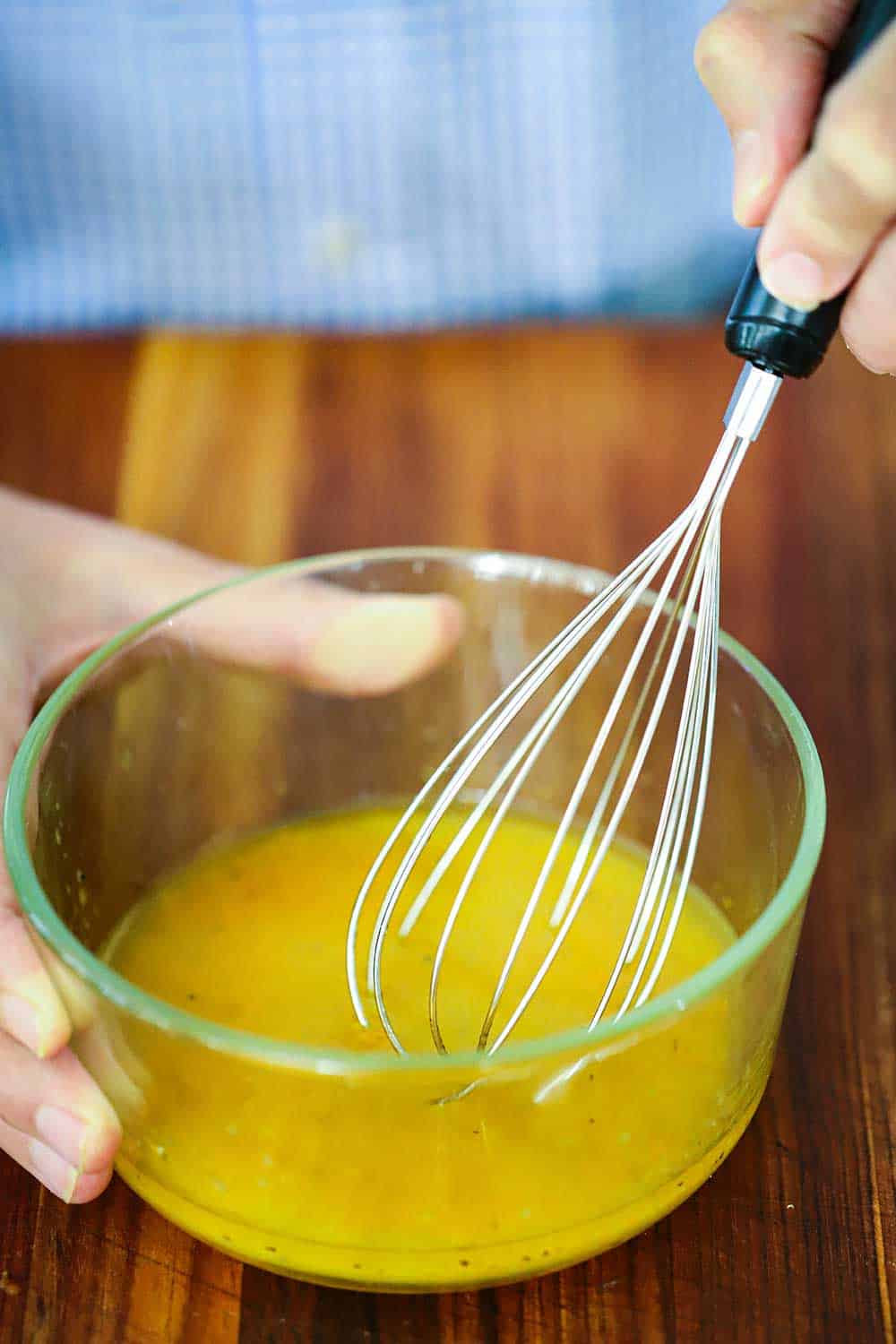 A small glass bowl filled with orange vinaigrette with a hand holding a whisk in it.