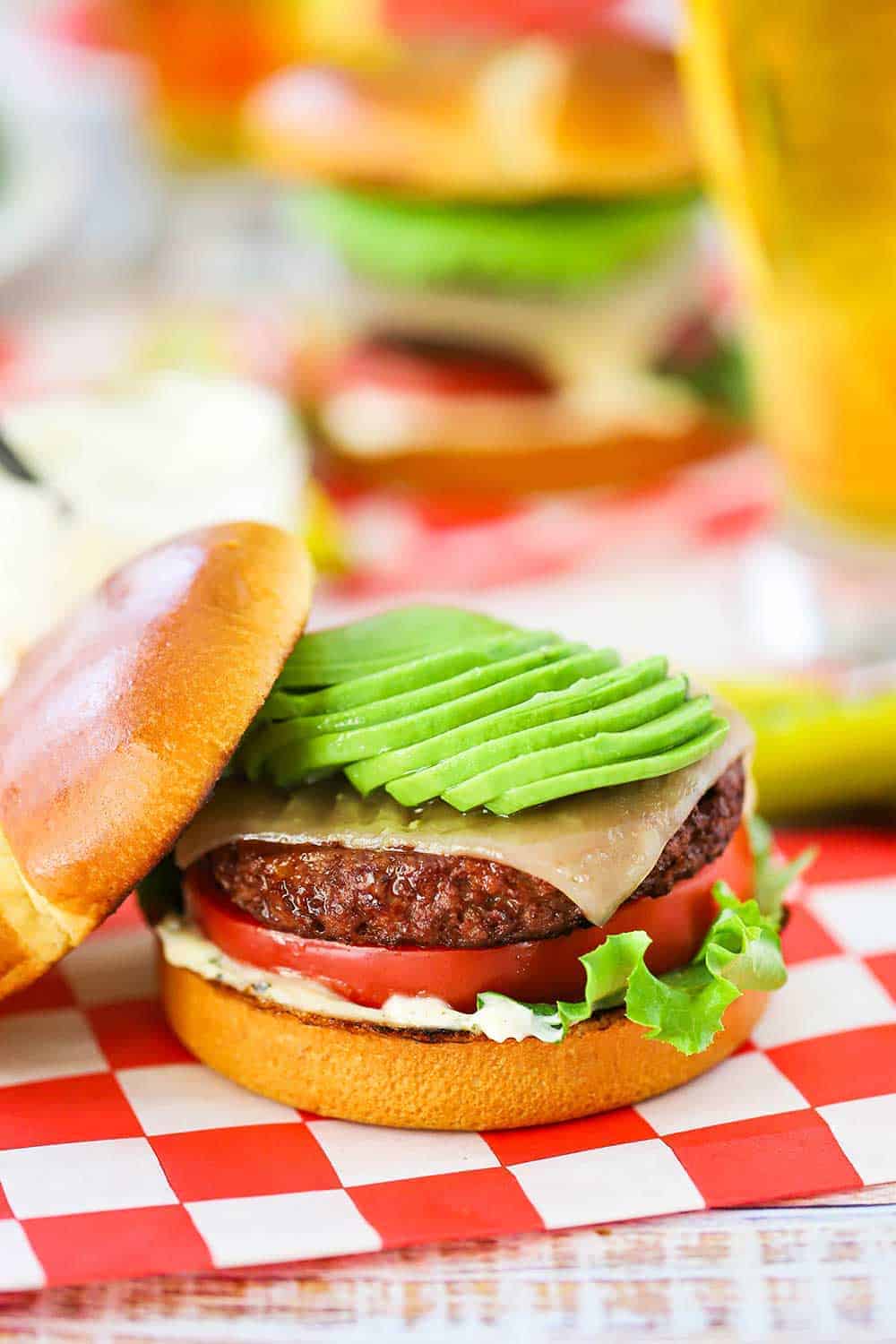 A plant-based California burger topped with sliced avocado sitting on a red-checkered napkin.