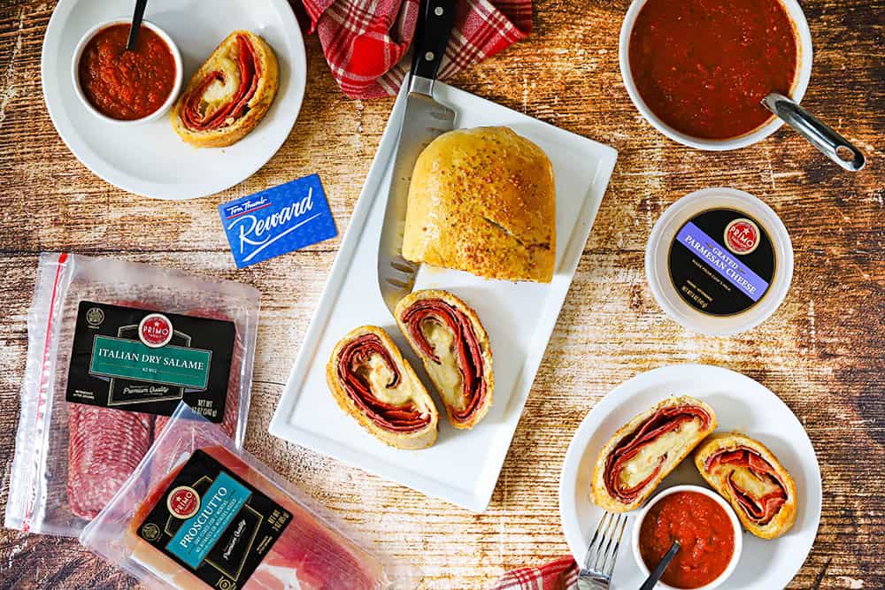 A sliced stromboli on a white platter with two pieces turned on their sides and next to individual plates of stromboli slices.