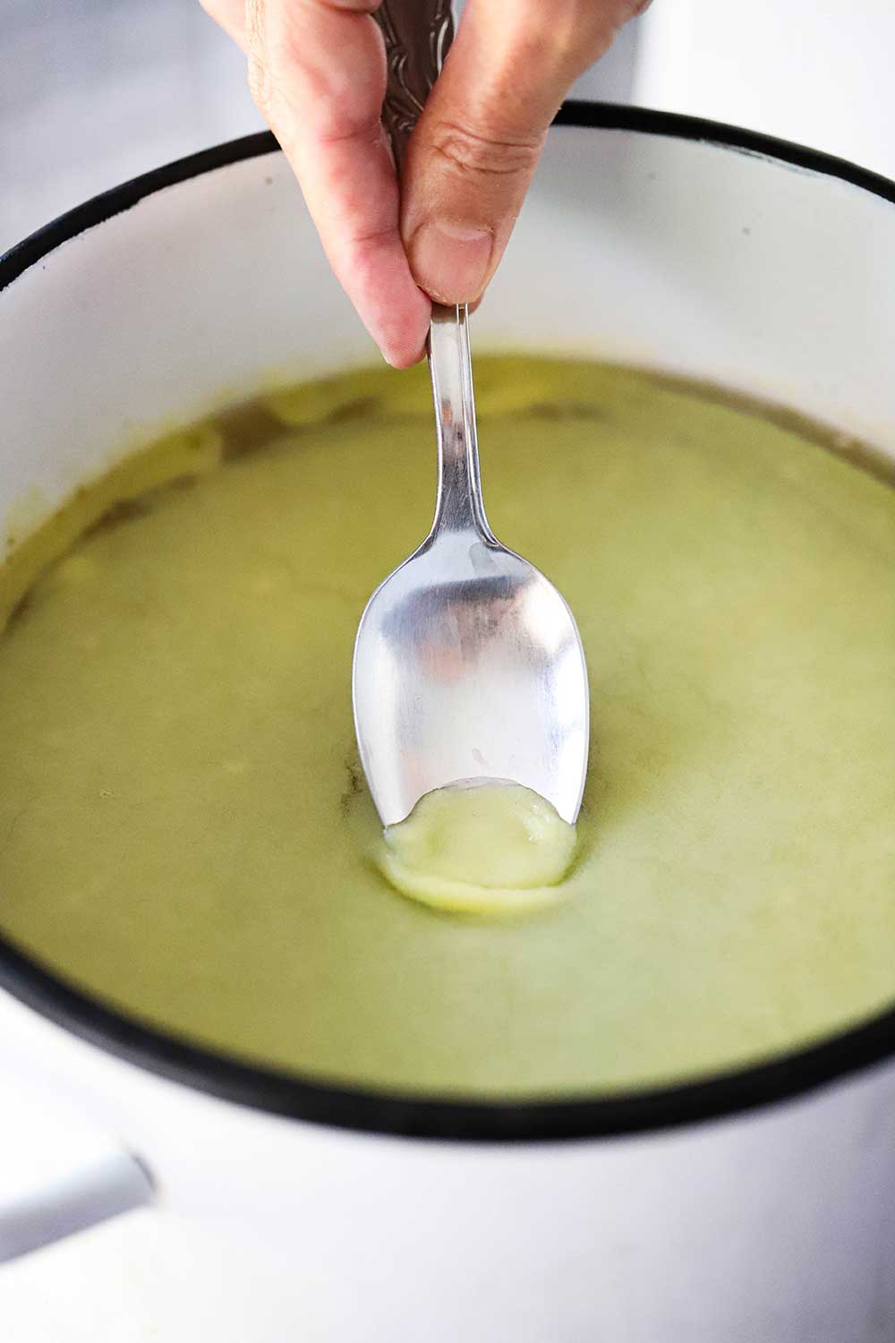 A hand using a spoon to skim congealed chicken fat from the surface of a pot filled with chilled chicken stock.