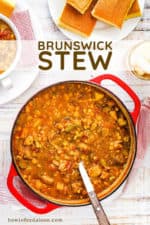 A large circular red Dutch oven filled with Brunswick stew with a large ladle placed in the pot.