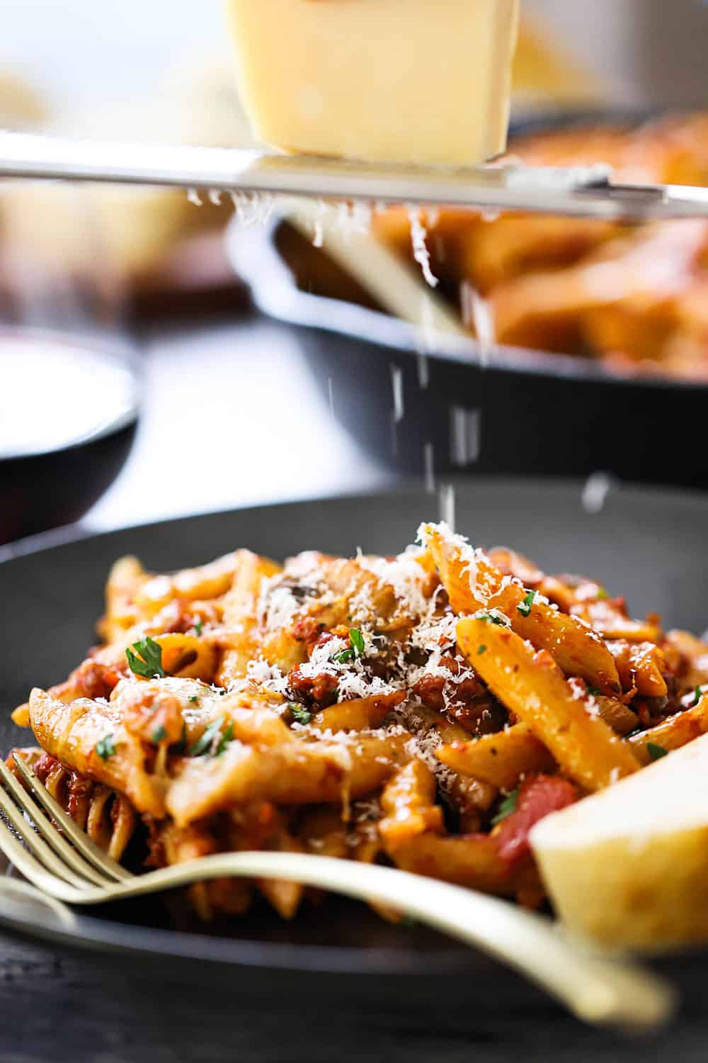 A block of Parmesan cheese being grated over a plate of vegetarian pasta.