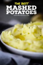 A white serving bowl filled with mashed potatoes with melted butter and ground black pepper on top.