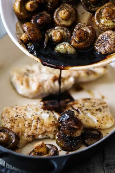 Cooked mushrooms in an agrodolce sauce being poured over seared haddock in a baking dish.