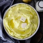A large circular bowl filled with mashed potatoes with melted butter on top.