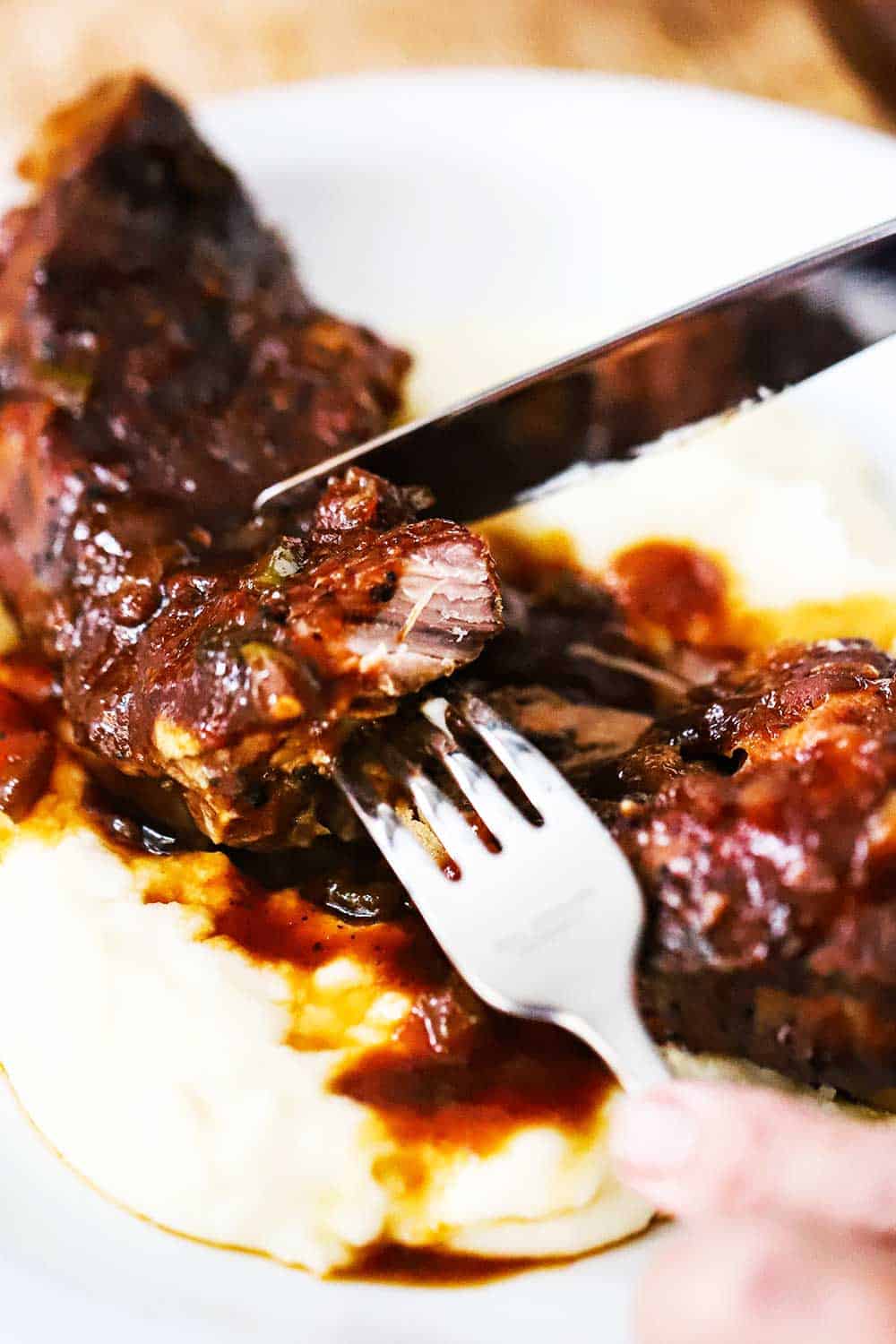 A fork and knife being used to cut into a tender country-style pork rib on a plate.