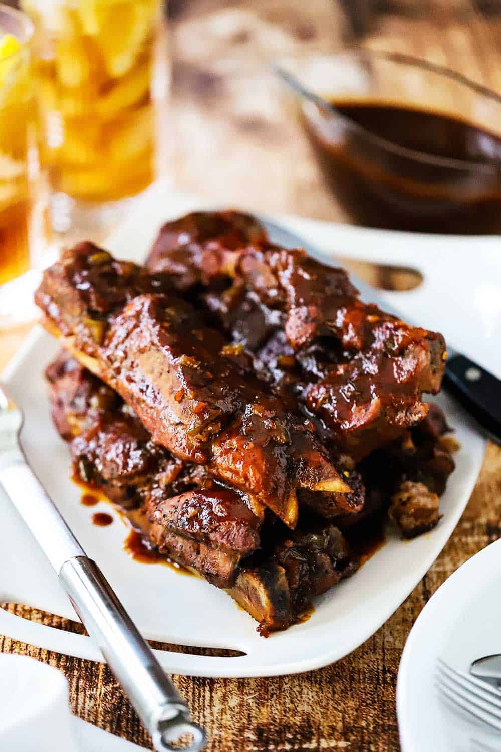 A white platter with a stack of country-style pork ribs next to two glasses of iced tea.
