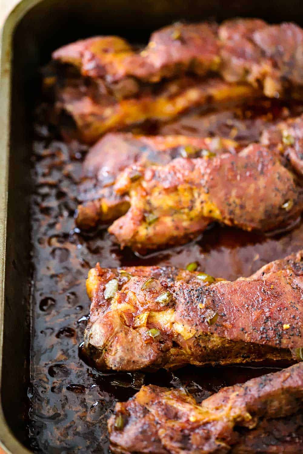A large roasting pan filled with country-style pork ribs with sauce in the pan.