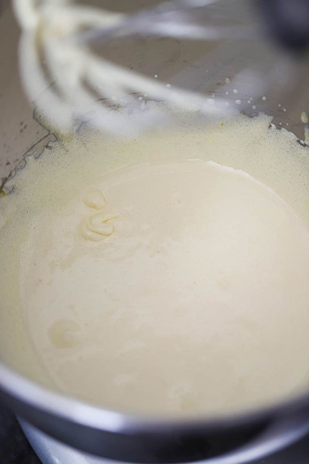 A stand-mixer bowl filled with a creamed egg mixture with the whisk attachment above the bowl.