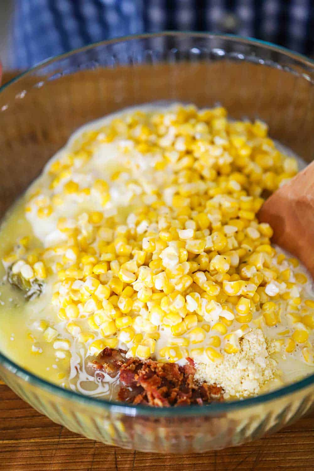 A large glass bowl filled with creamed corn, chopped bacon, corn muffin mix, and green chilies.