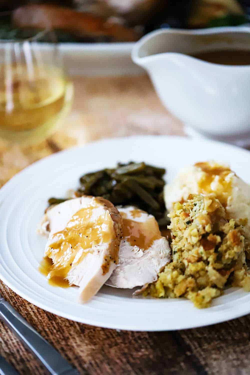 A white plate filled with carved turkey, stuffing, mashed potatoes, and green beans all topped with gravy.