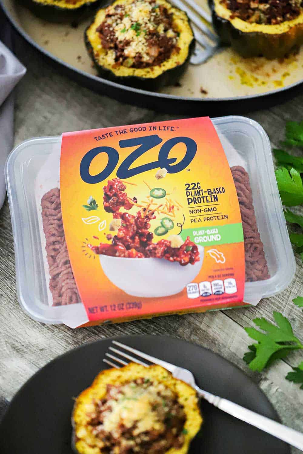 A package of OZO Protein-Based Ground in between a plate and baking dish filled with stuffed acorn squash.