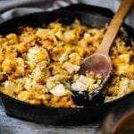 A large black cast-iron skillet filled with turkey and stuffing dressing with some of the food scooped out.
