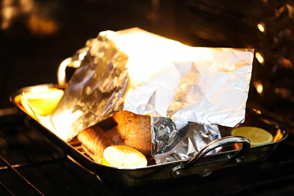 A large piece of foil sitting on top of a turkey in a roasting pan inside an oven.