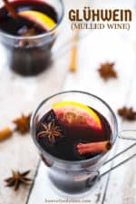 Two clear glasses filled with mulled wine and garnished with a cinnamon stick, star anise, and an orange slice.
