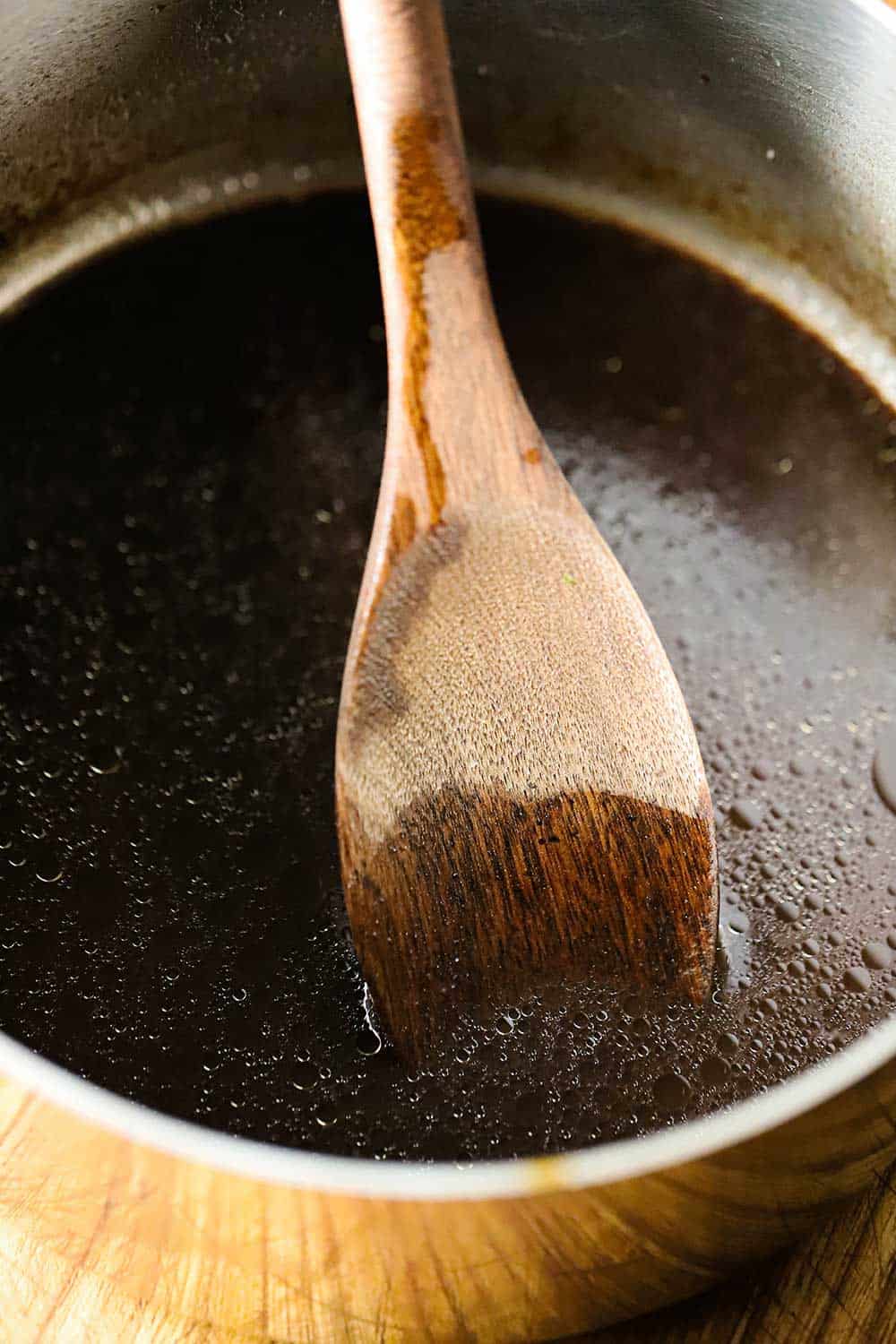 A saucepan filled with homemade au jus sauce with a wooden spoon in it.
