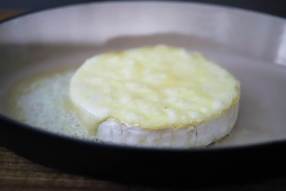 A wheel of brie that has been baked in a baking dish and is bubbling on the surface.