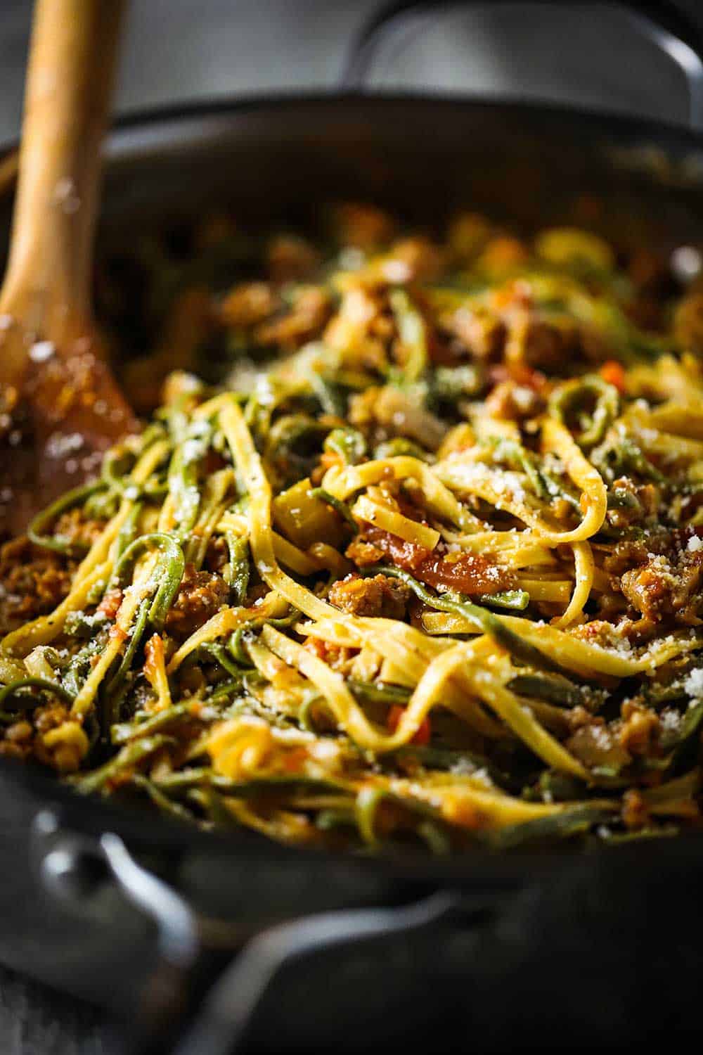 A large skillet filled with fettuccine with creamy sausage sauce with a wooden spoon also in the pan.