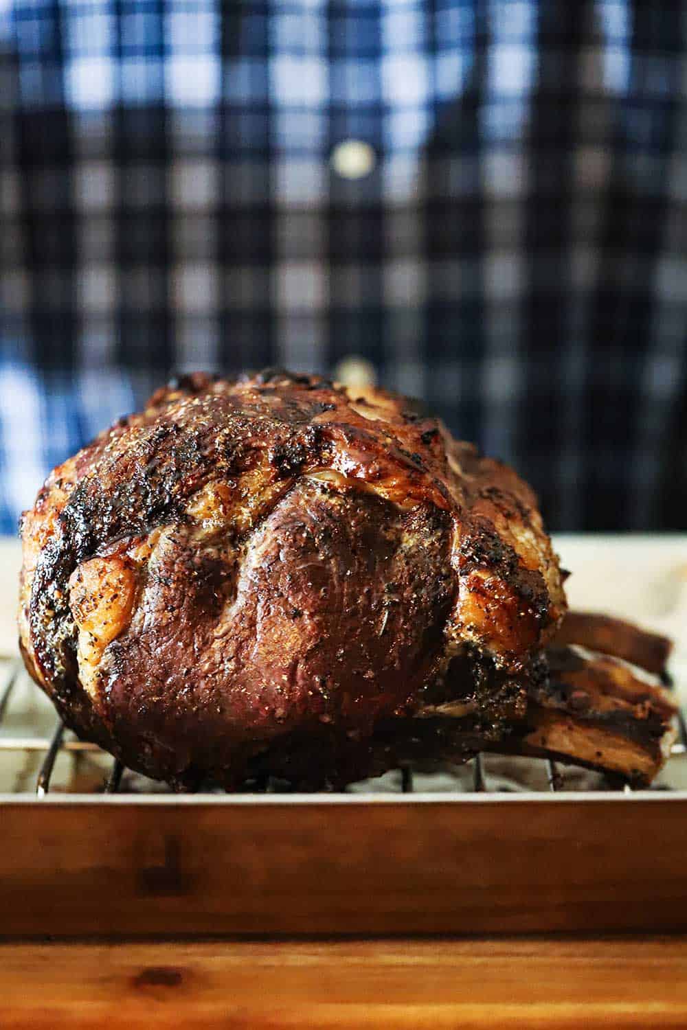 A standing prime rib roast fully cooked in a roasting pan on a cutting board.