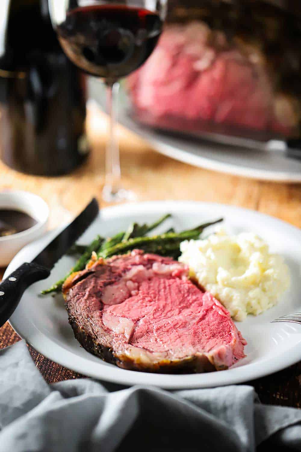 A white dinner plate filled with a slice of roast beef next to helping of mashed potatoes and green beans.