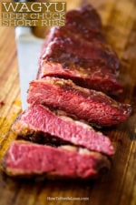 A cut of Wagyu chuck short ribs on a cutting board that has been cut into slices all sitting on top of the chef's knife.