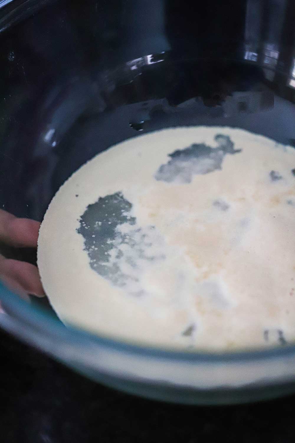 A glass bowl with about 1 cup of warm water in it with yeast foaming on top of it.