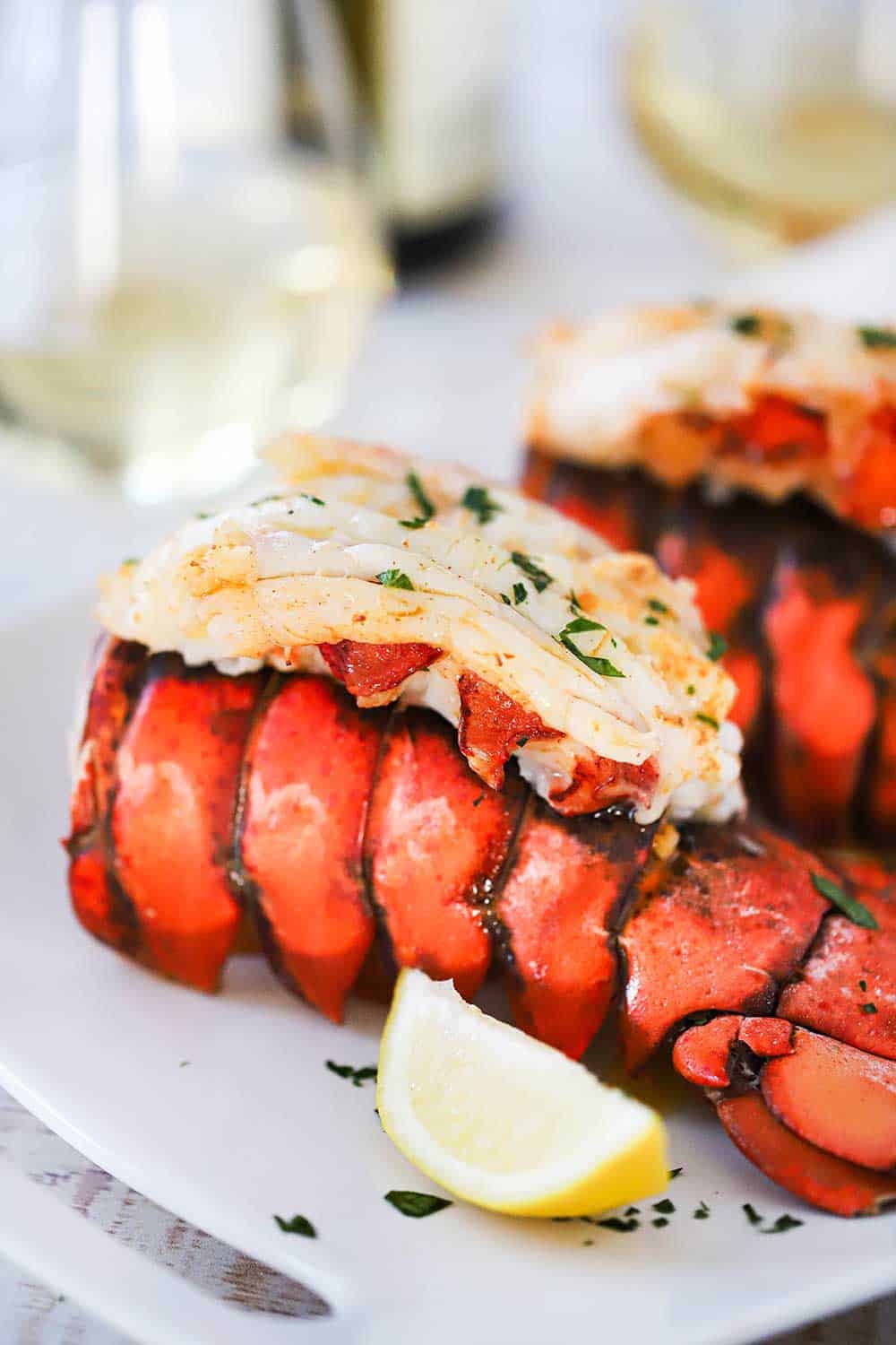 An 8 oz. fully cooked lobster tail with the meat sitting on top of the tail all on a white dinner plate with a lemon wedge.