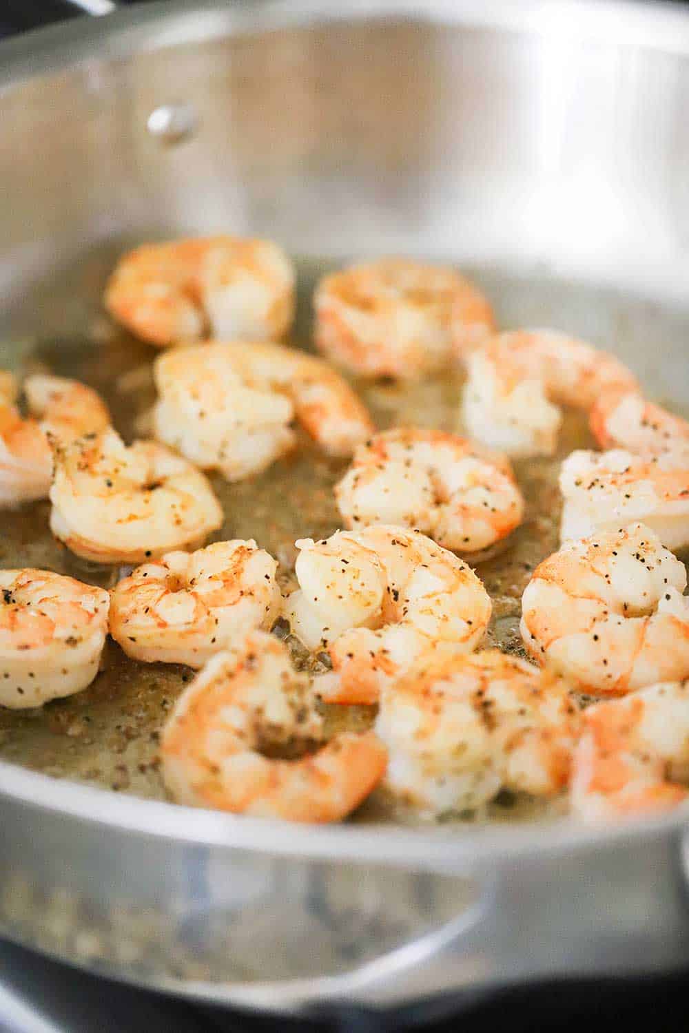 A large stainless steel skillet filled with cooked shrimp seasoned with salt and pepper.