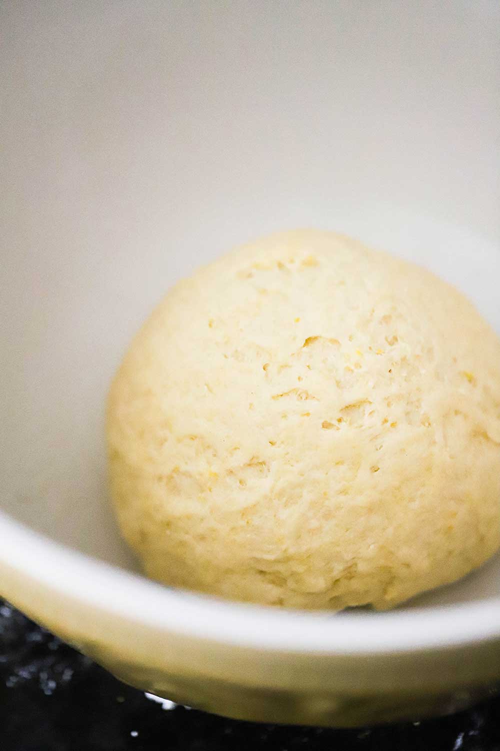 A ball of pizza dough in a ceramic bowl just before it is to begin the proofing process.