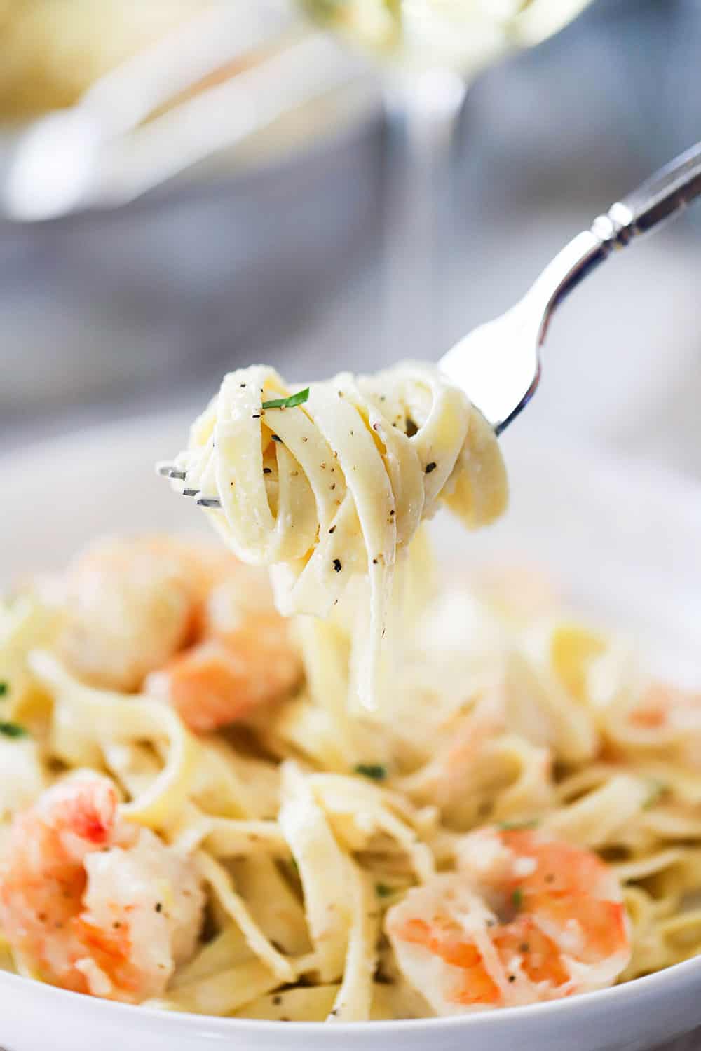 A fork being held up with fettuccine alfredo wrapped around the ends of it, over a bowl of the same.