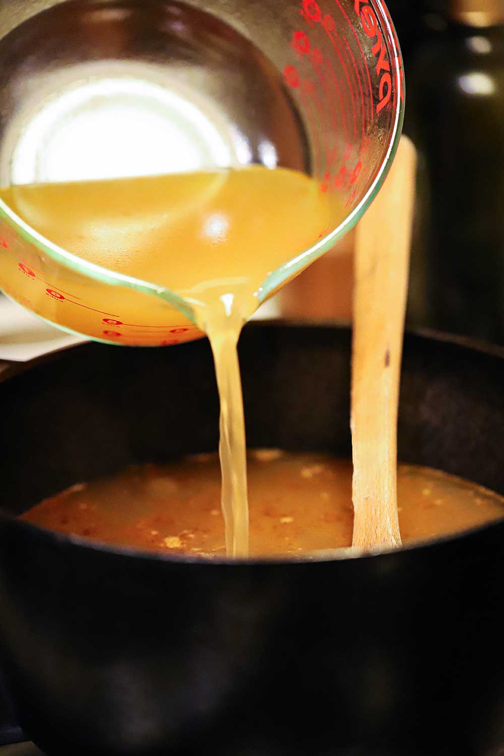 A large measuring cup is being used to pour shellfish stock into a pot of shrimp gumbo.