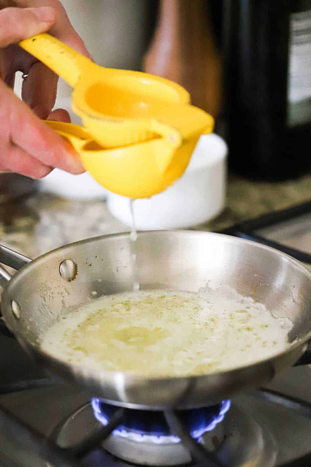 A person using a citrus press to squeeze fresh lemon juice into a small saucepan filled with melted butter.